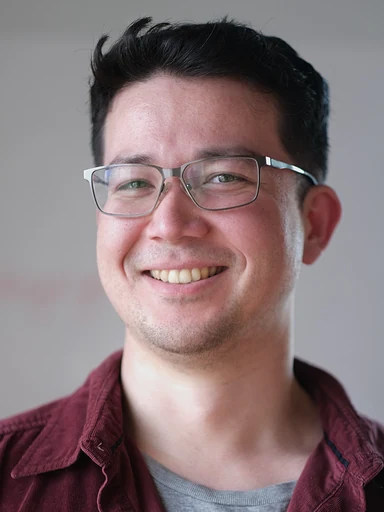 眼鏡をかけ、えんじ色のシャツで微笑むエリック・モックラー